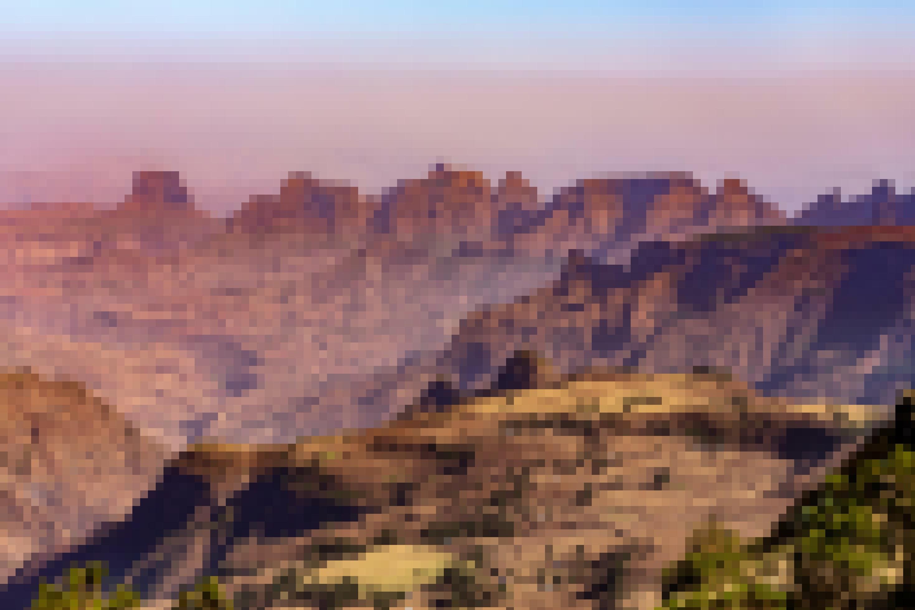 Eine trockene Gebirgslandschaft mit zackigen Gipfeln, im Vordergrund eine kleine bäuerliche Siedlung.