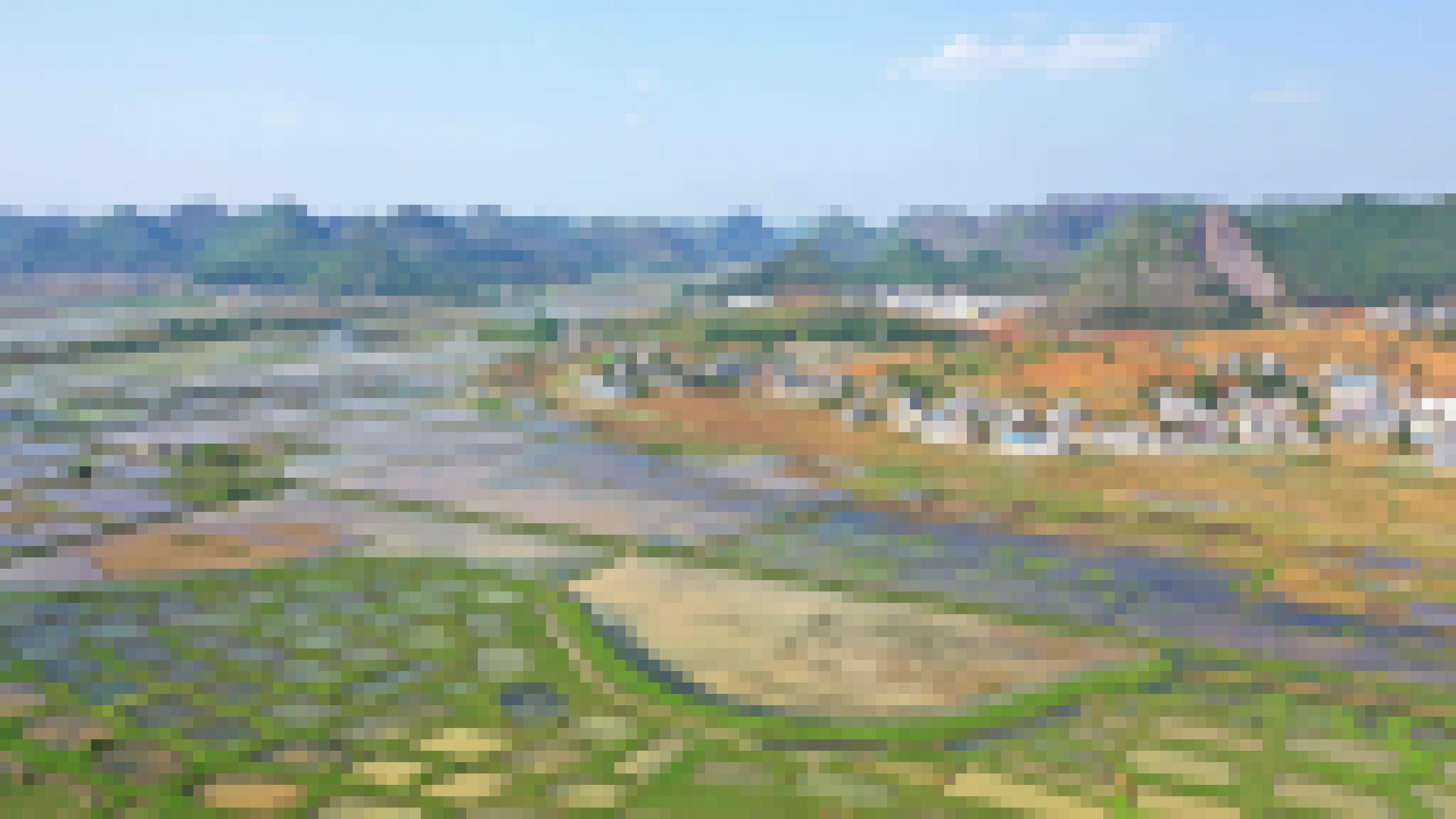 Eine Landschaft mit zahlreichen kleinen Tümpeln vor einem Dorf und Hügeln.