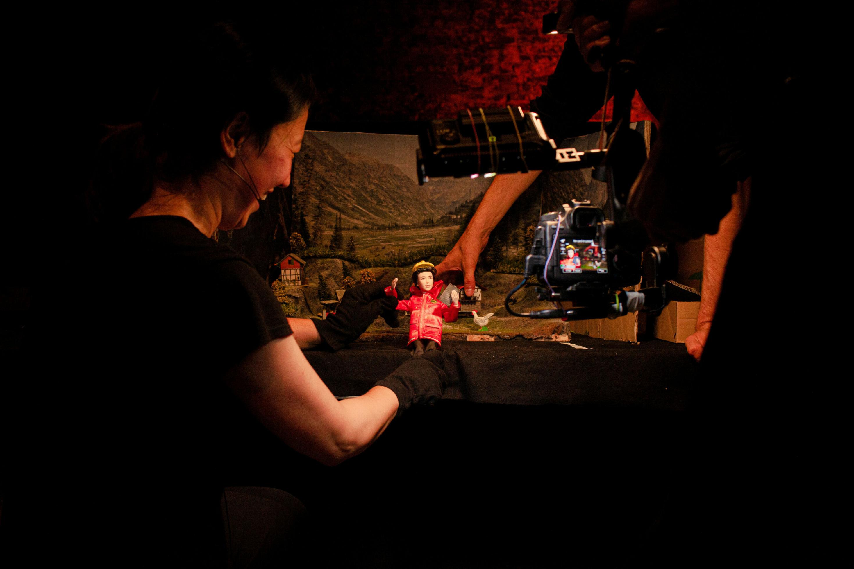 Eine Darstellerin bewegt eine Puppe durch eine Modell-Landschaft, ein Darsteller filmt die Szene.
