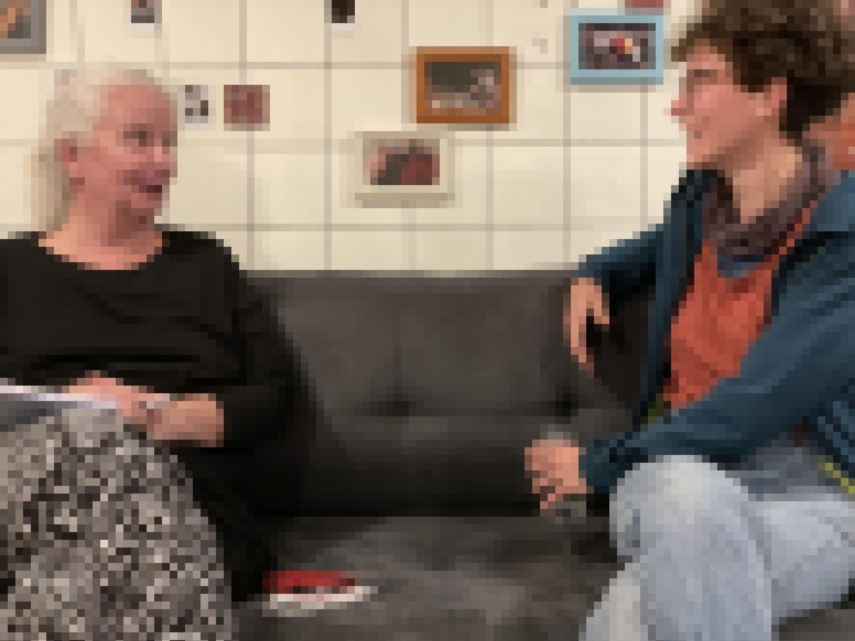 Die beiden Regisseurinnen Barbara Kölling und Clara Gohmert sitzen sich auf einer Couch gegenüber und unterhalten sich. Im Hintergrund weiße Kacheln und viele kleine, gerahmte Bilder.