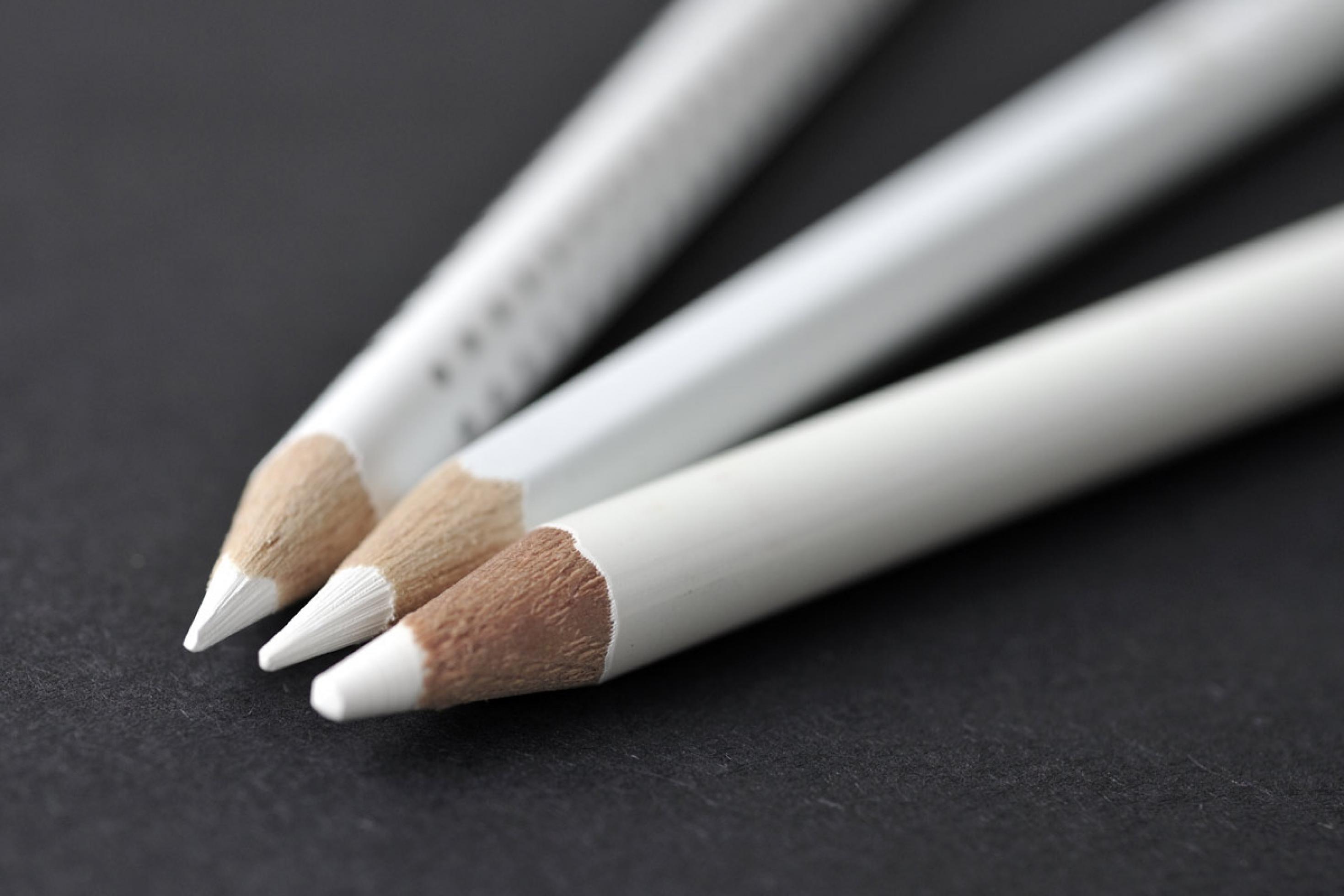 Drei Bleistifte mit weißer Mine, die der Reinzeichnung auf schwarzem Karton dienen