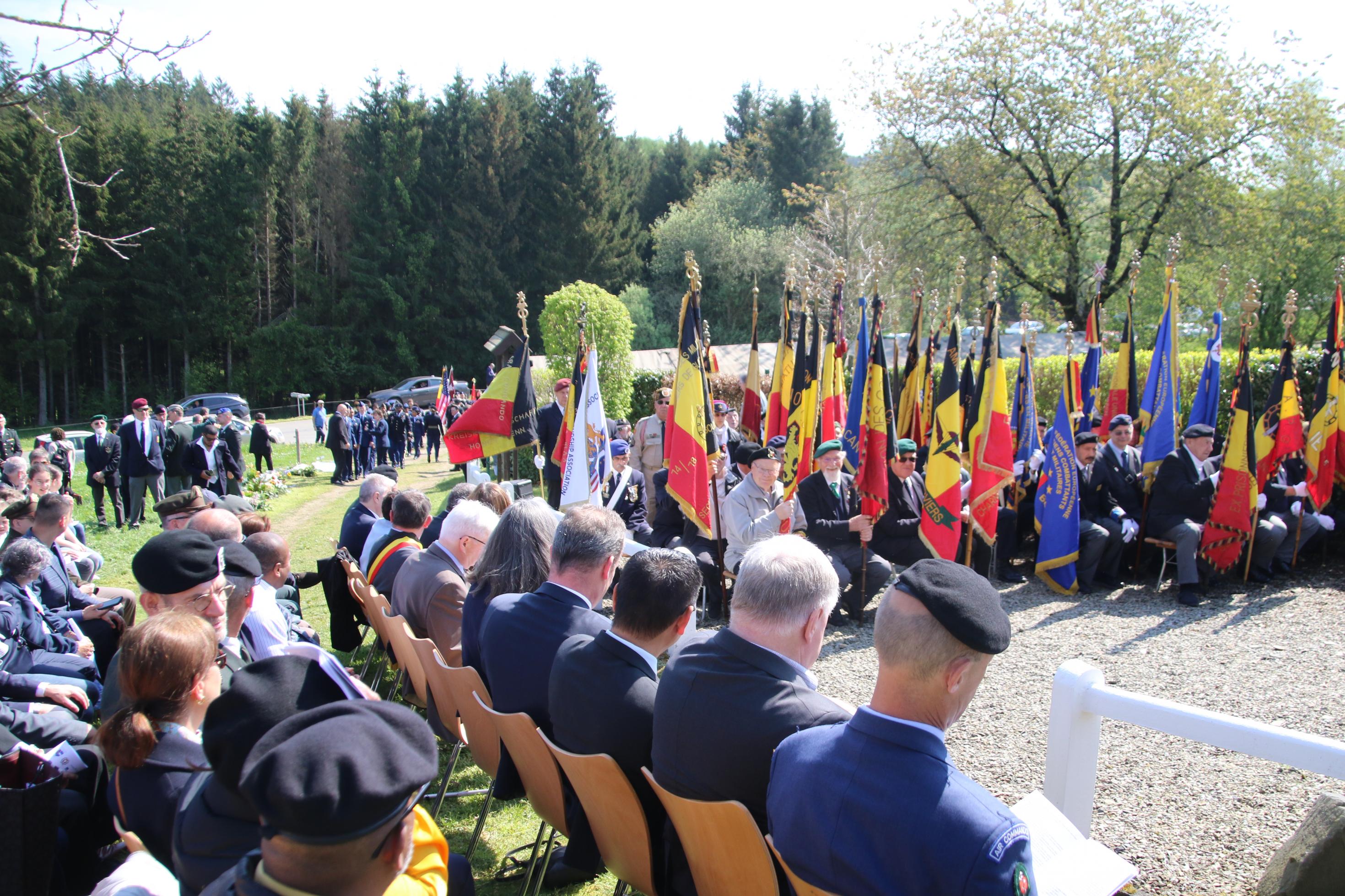 Personen in Uniformen und Anzügen sitzen auf Stühlen vor dem Gedenkstein.