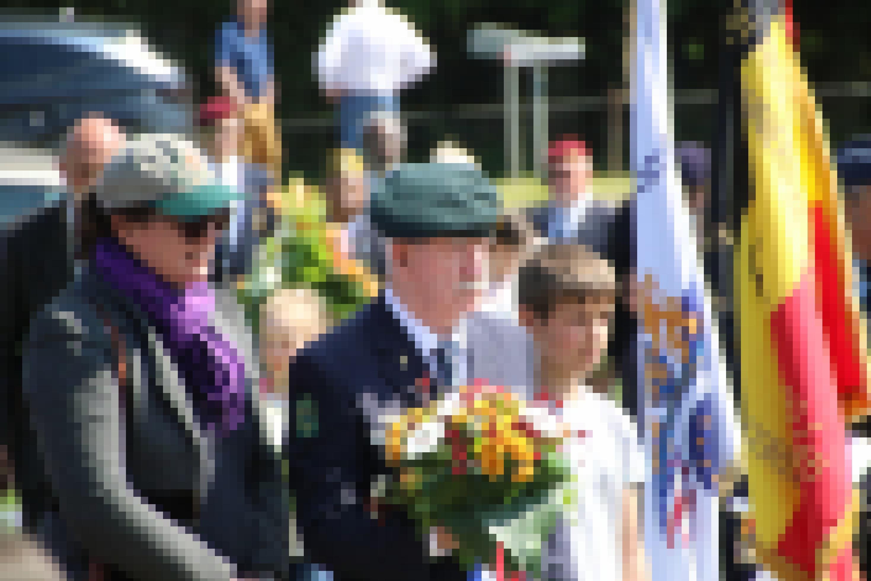 Ein älterer Herr in Uniform hält einen Blumenkranz in der Hand.