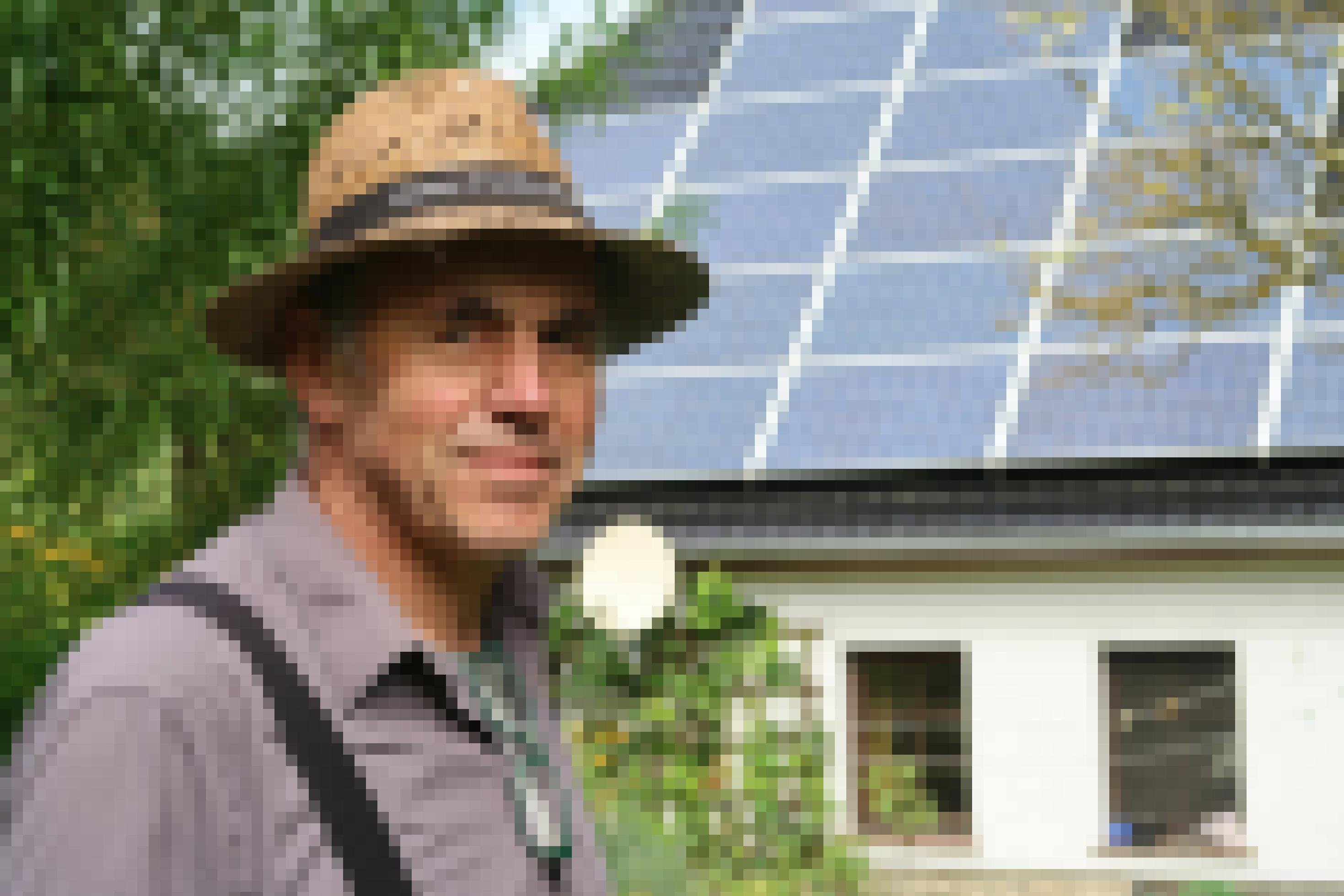 Mann mit Strohhut, im Hintergrund ein Hausdach mit Solarzellen.