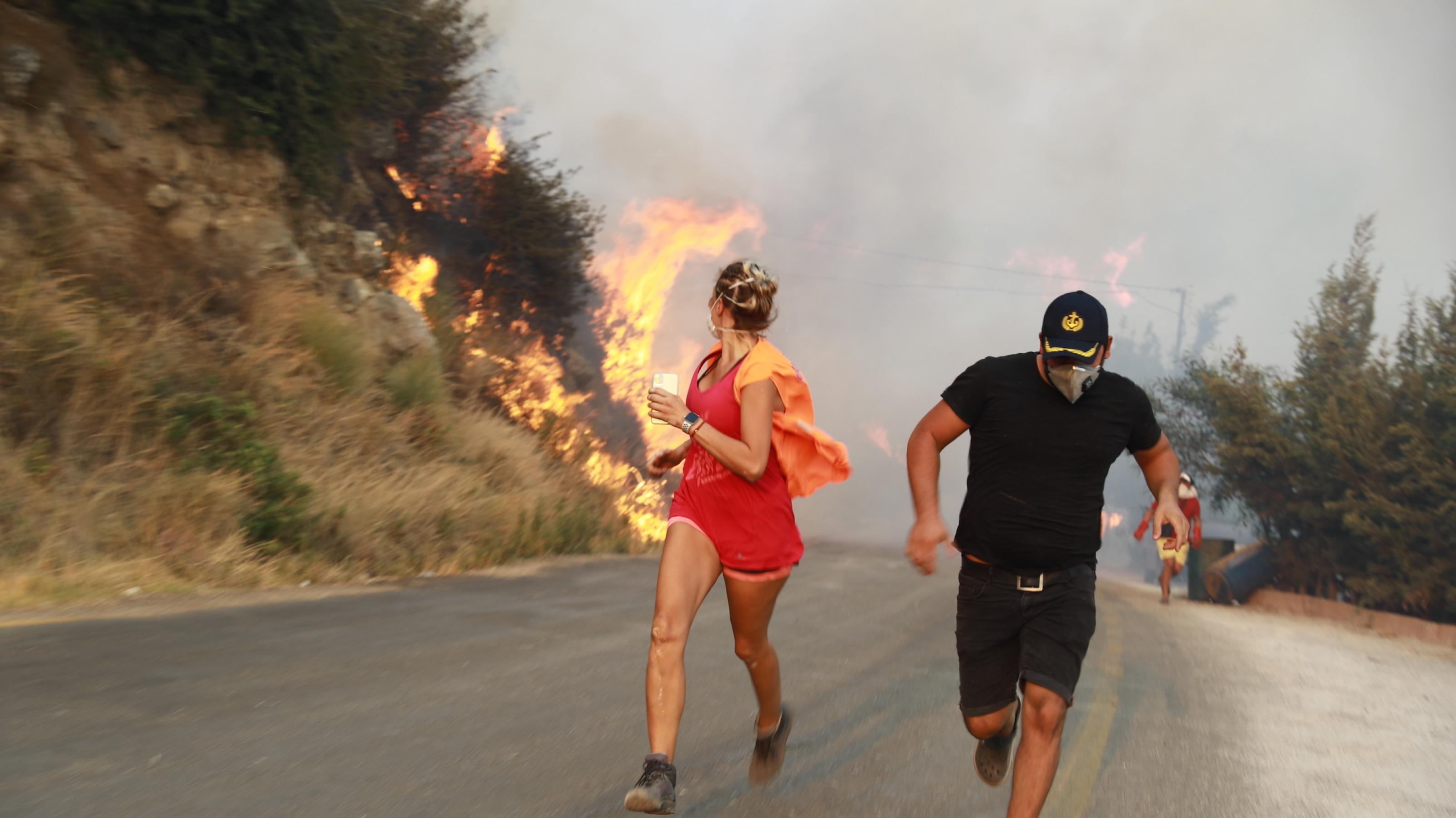 Ein Mann und eine Frau laufen auf einer Landstraße vor dem Feuer davon