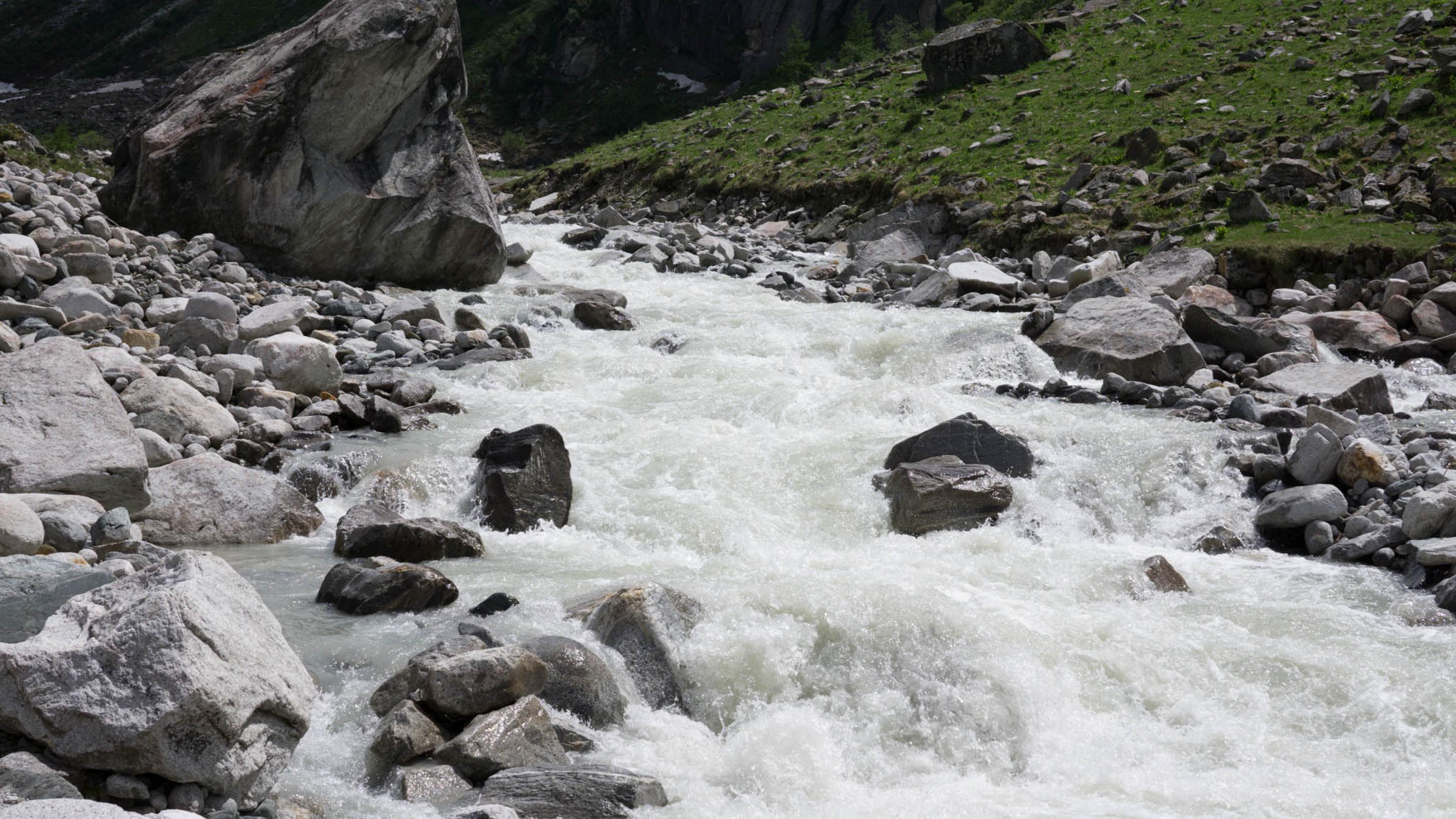 Gletscherbach mit großen Steinen und wild tosendem Wasser.