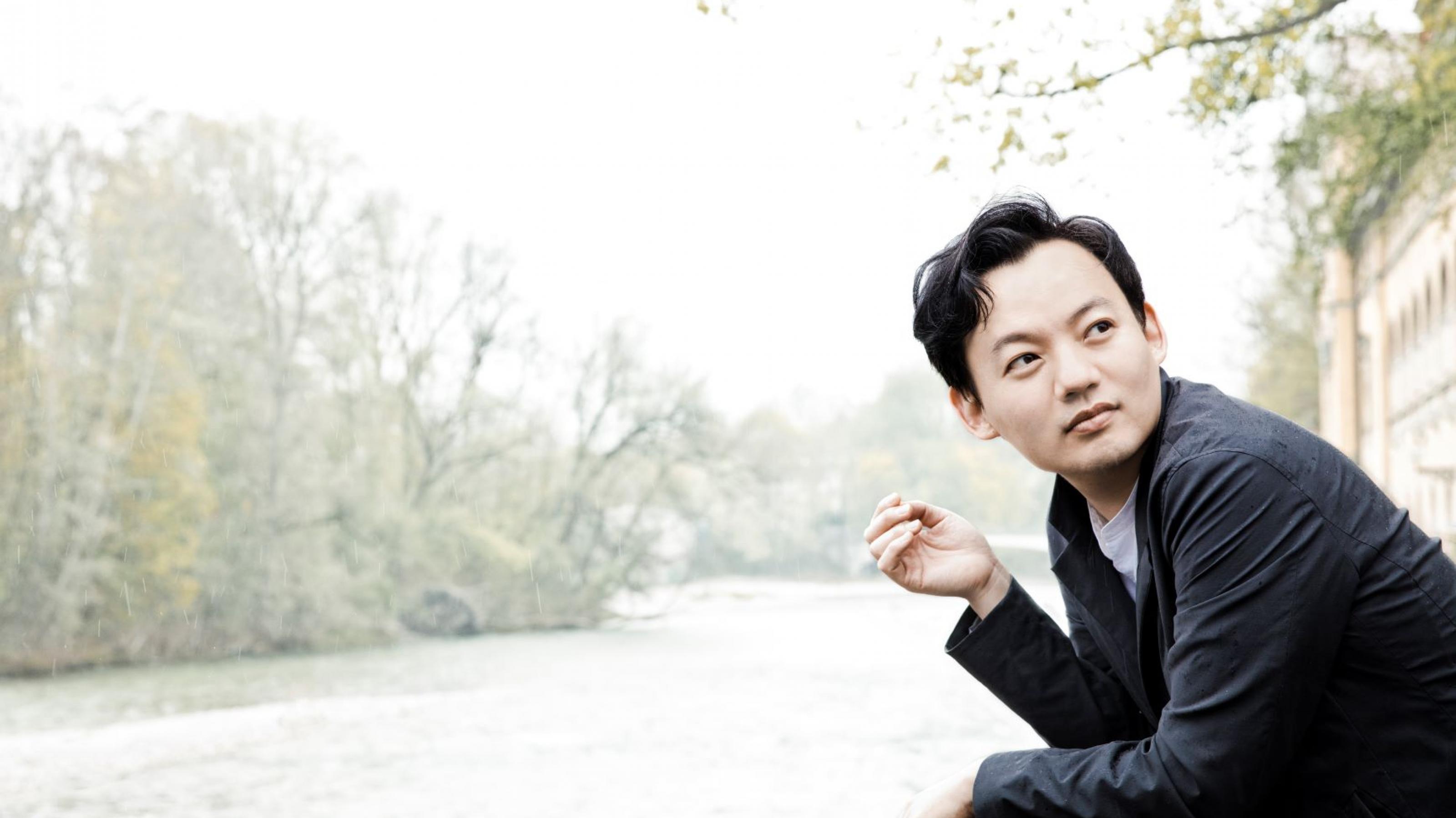 Der junge, in Seoul geborene Pianist William Youn steht auf eine Mauer gestützt an einem Fluss.