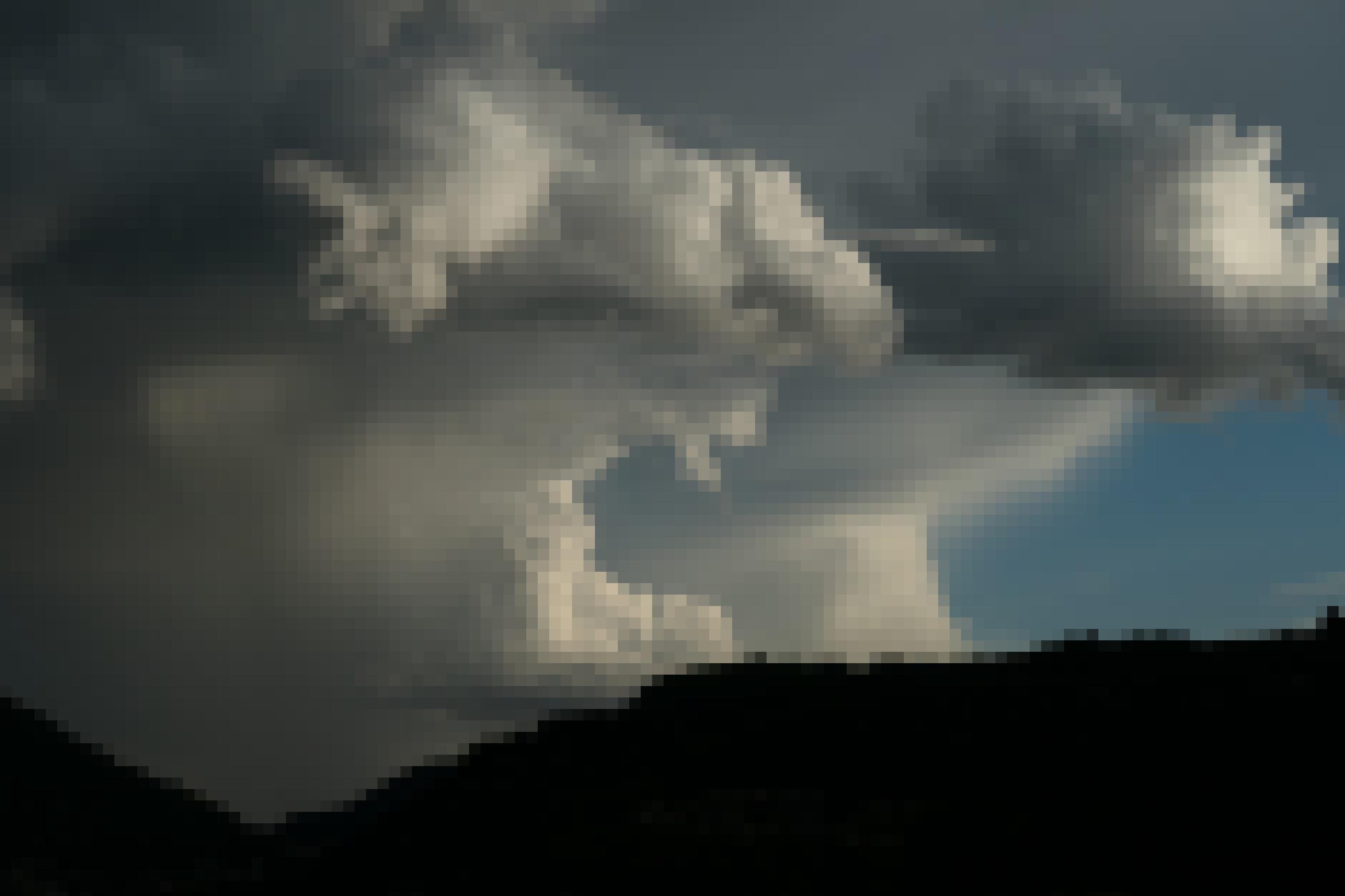 Über der Silhouette einer Bergkette türmen sich mächtige Wolkenformationen, links düster und grau, rechts heller und ein Stück Himmel frei lassend. In der Mitte erinnern die Wolken ein wenig an ein riesiges Maul, das den freundlichen blauen Himmel rechts zu verschlingen droht.