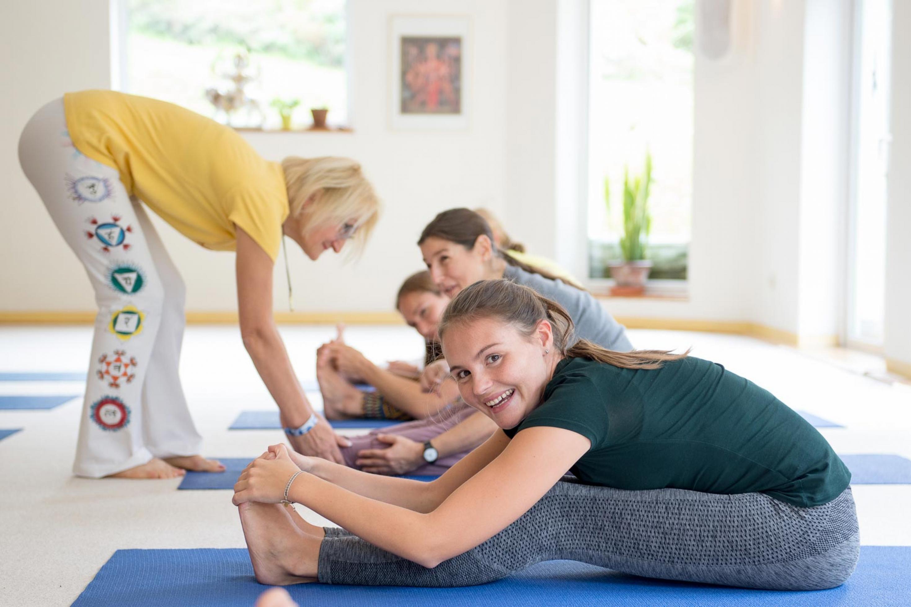 Mehere Frauen werden von einer Ygoa-Lehrerin beim Yoga angeleitet.