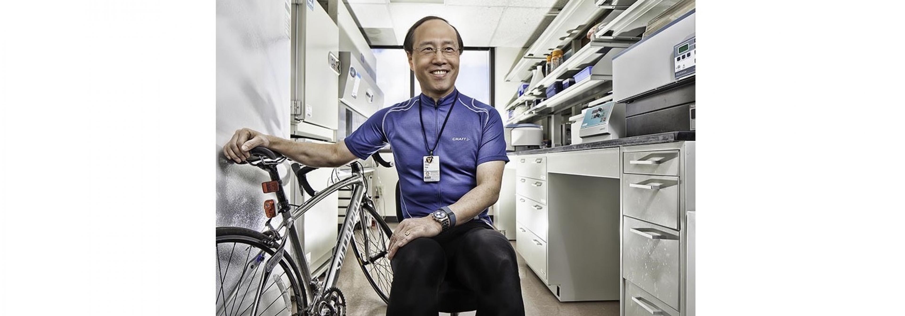 Ein sportlicher mittelalter Wissenschaftler in seinem Labor. Er hat ein Fahrradtrikot an. Neben ihm steht sein Rennrad.