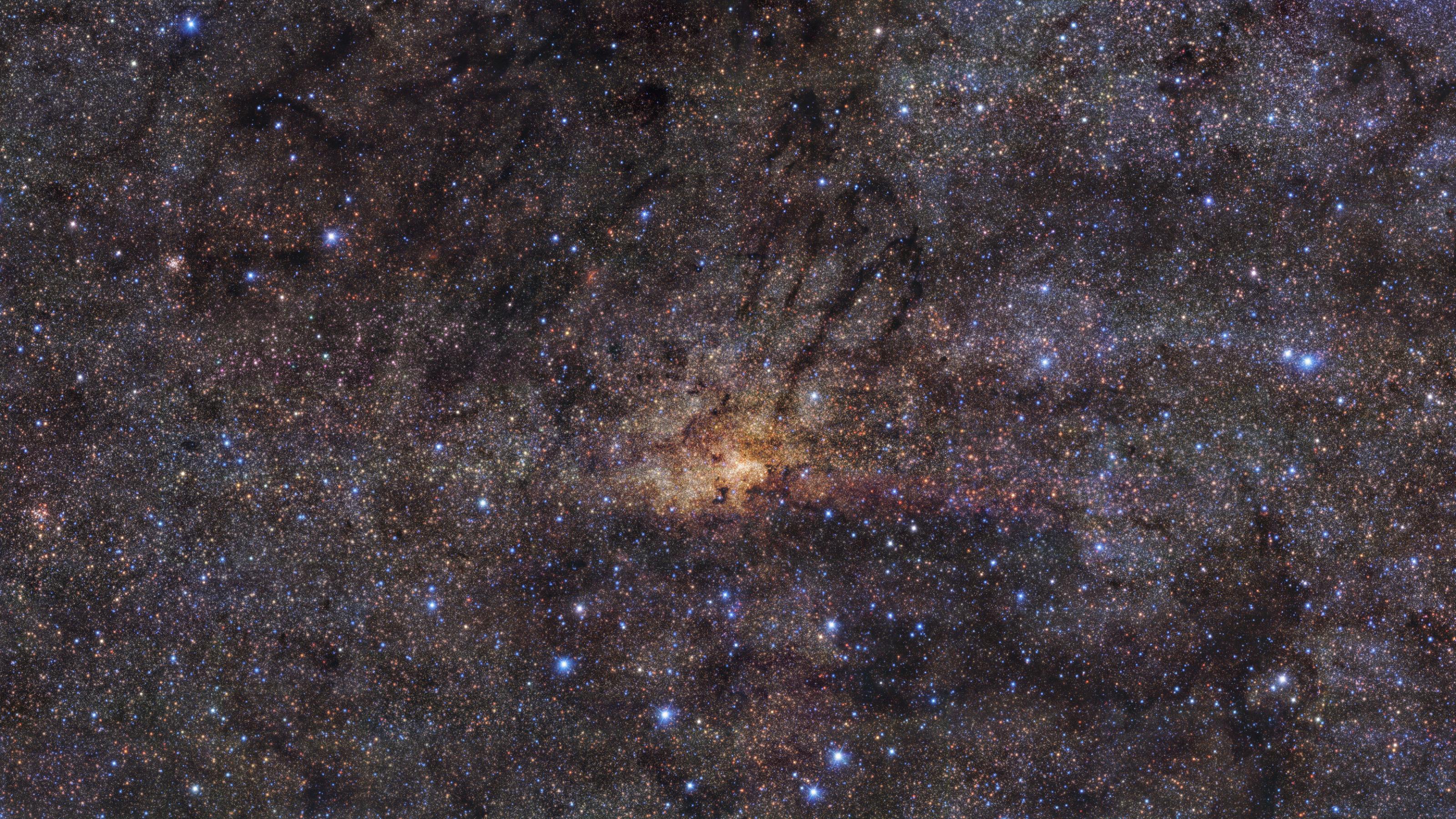 Das Foto zeigt ein aktuelles Bild vom Zentrum unserer Milchstaße. Zu sehen ist eine riesige Menge von Sternen vor schwarzem Hintergrund, in denen sich nur wenige größere Strukturen erkennen lassen, sowie Gas- und Staubwolken. In der Mitte konzentrieren sich mehr Sterne und die Farbtönung ist gelblicher. Wissenschaftler der ESO können durch Analyse des Bildes erkennen, dass die Sterne im Zentrum der Galaxis in mehreren Phasen entstanden sind, zwischen denen Jahrmilliarden lange Pausen lagen. Das Foto wurde vom Very Large Telescope der ESO in der chilenischen Atacama-Wüste aufgenommen.