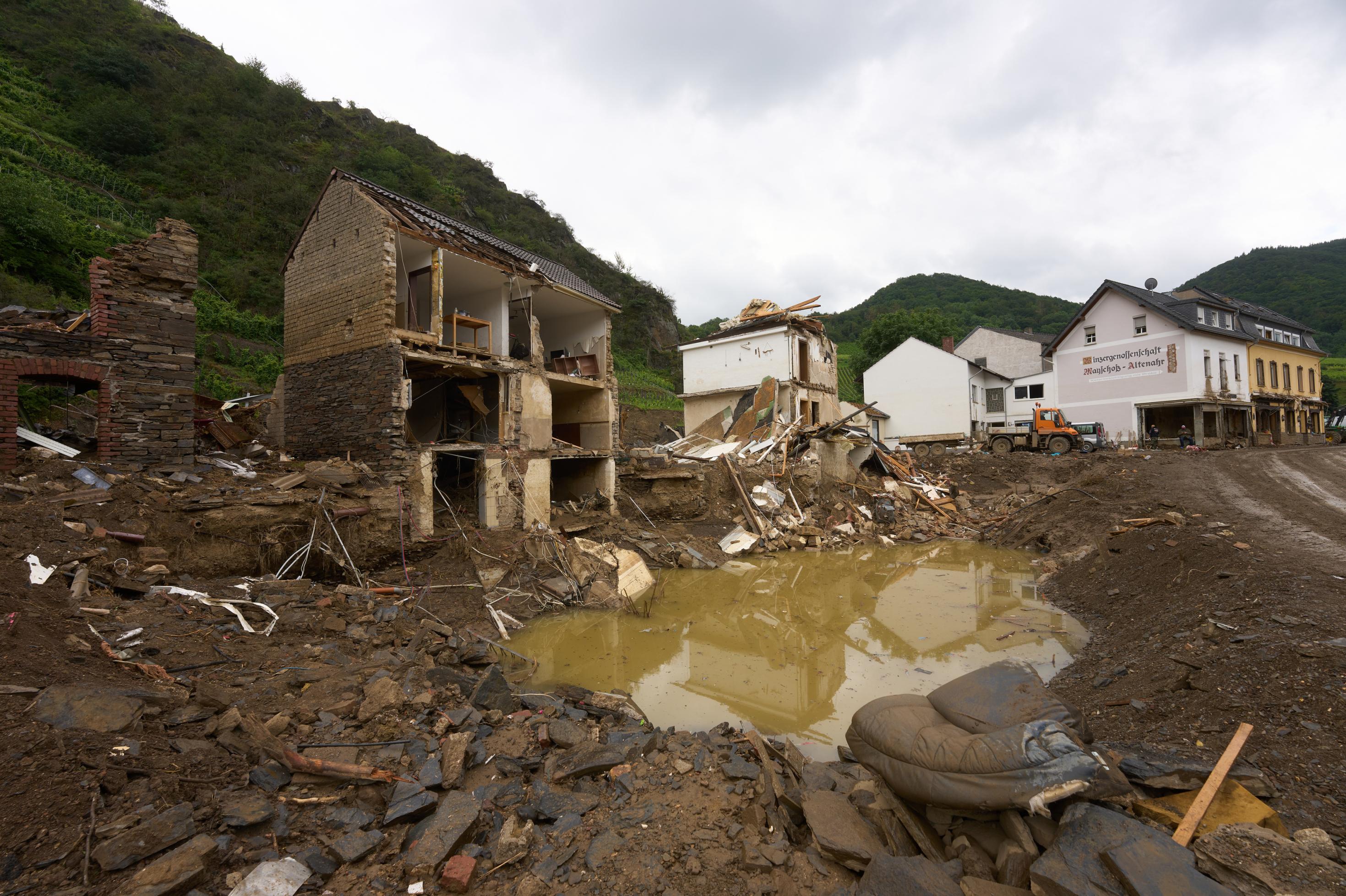 Haus, dessen Vorderfront vom Hochwassers zerstört wurde, im Vordergrund eine kraterförmige Pfutze, gefüllt mit Wasser