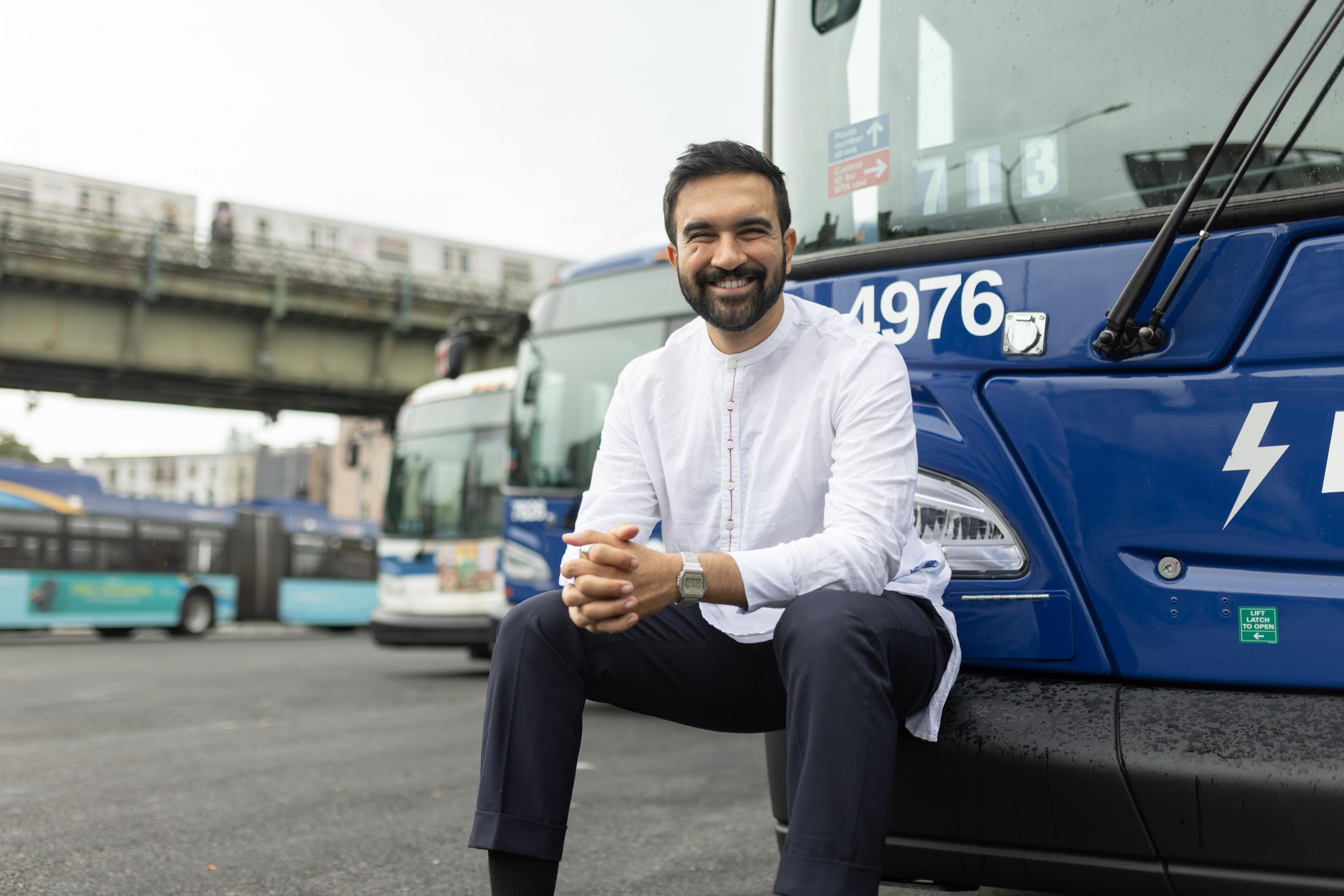 Der New Yorker Bürgermeister Zohran Mamdani sitzt auf der Stoßstange eines Stadtbusses.