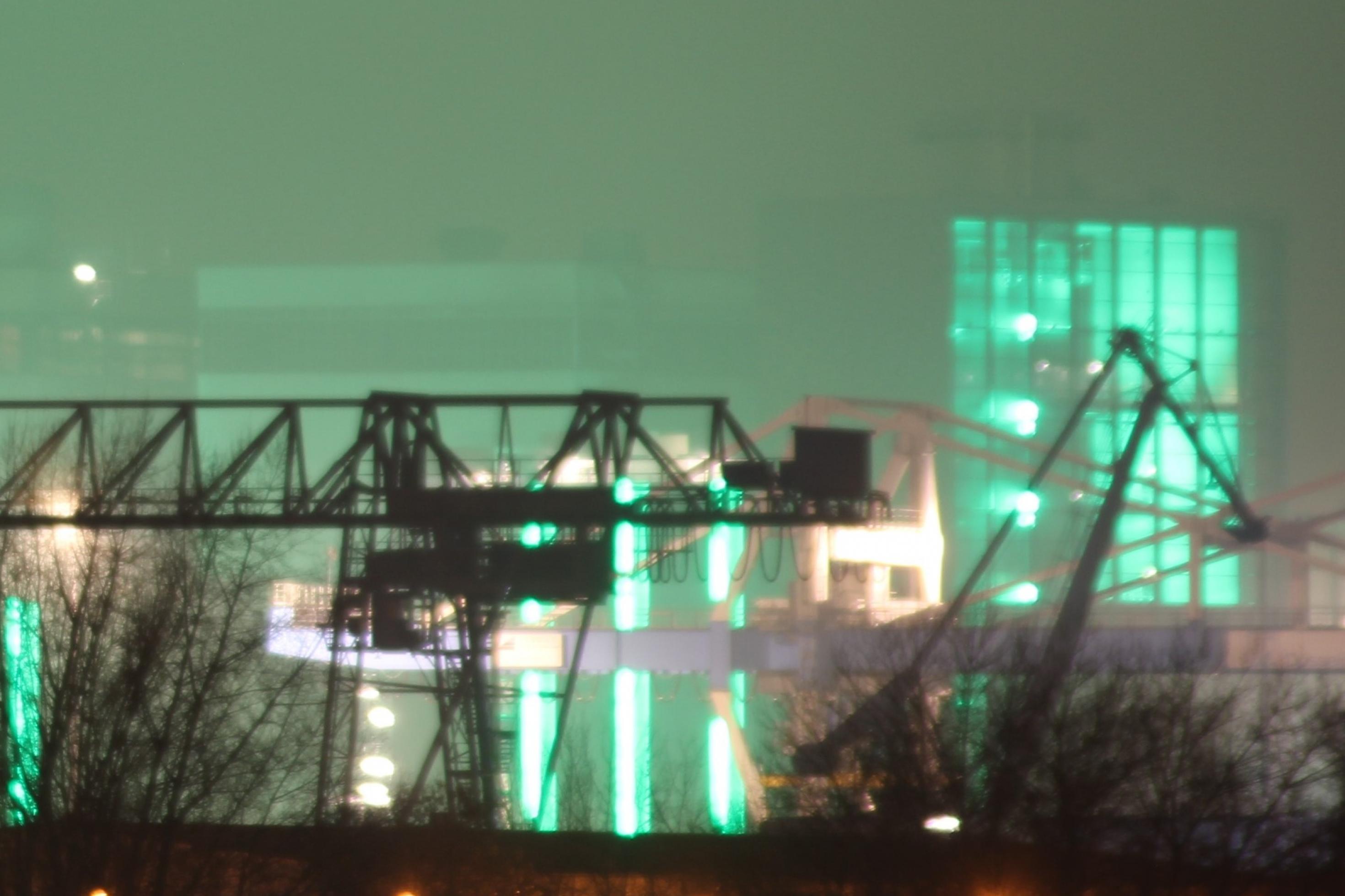 Industriekulisse:  Die Kräne des Düsseldorfer Hafens werden grün beleuchtet