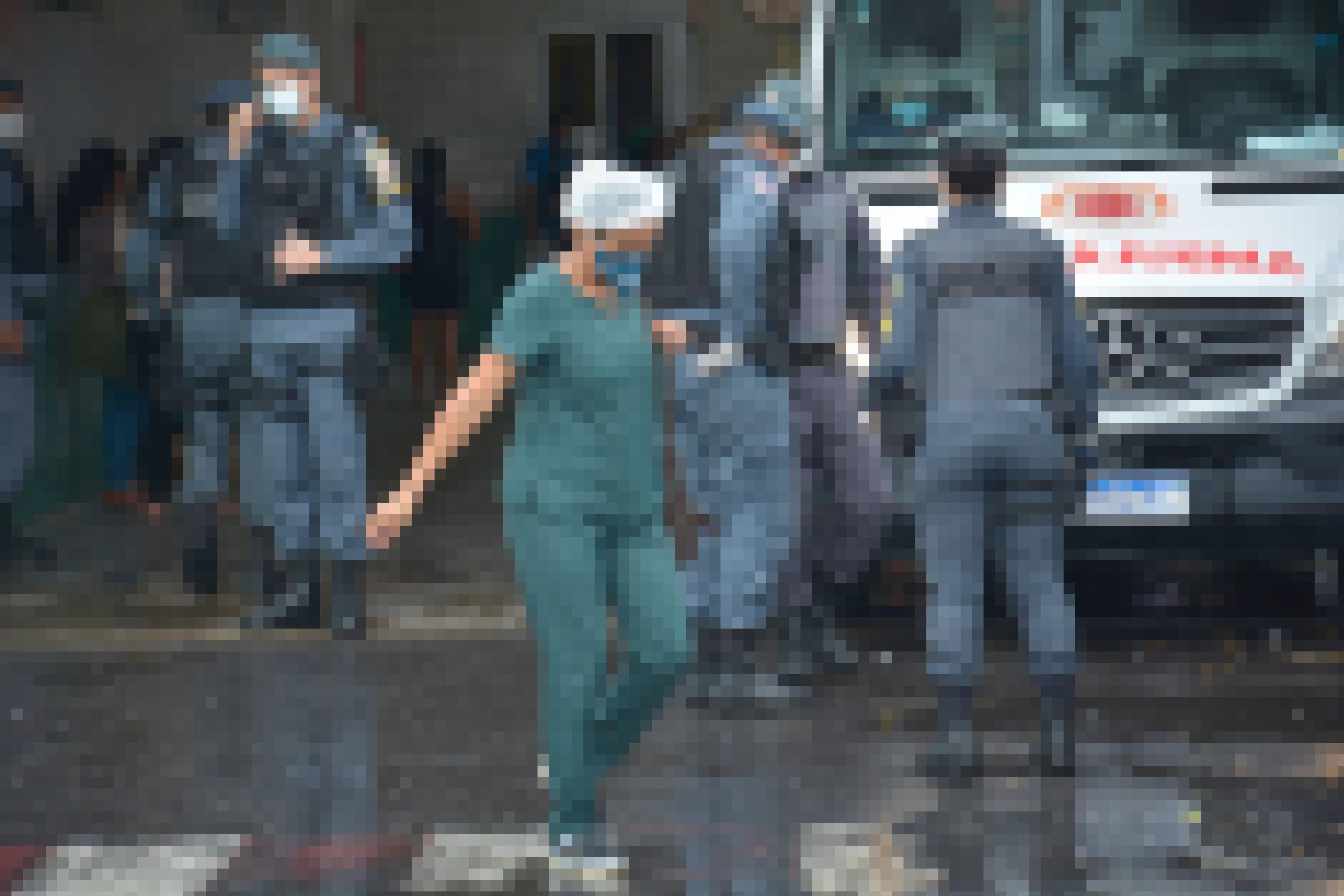 Vor dem Krankenhaus parkt ein Krankenwagen, der die mit Covid infizierten Patienten abtransportieren soll. Darum stehen fünf Personen der Militärpolizei und eine Krankenschwester läuft über den regennassen, spiegelnden Asphalt.