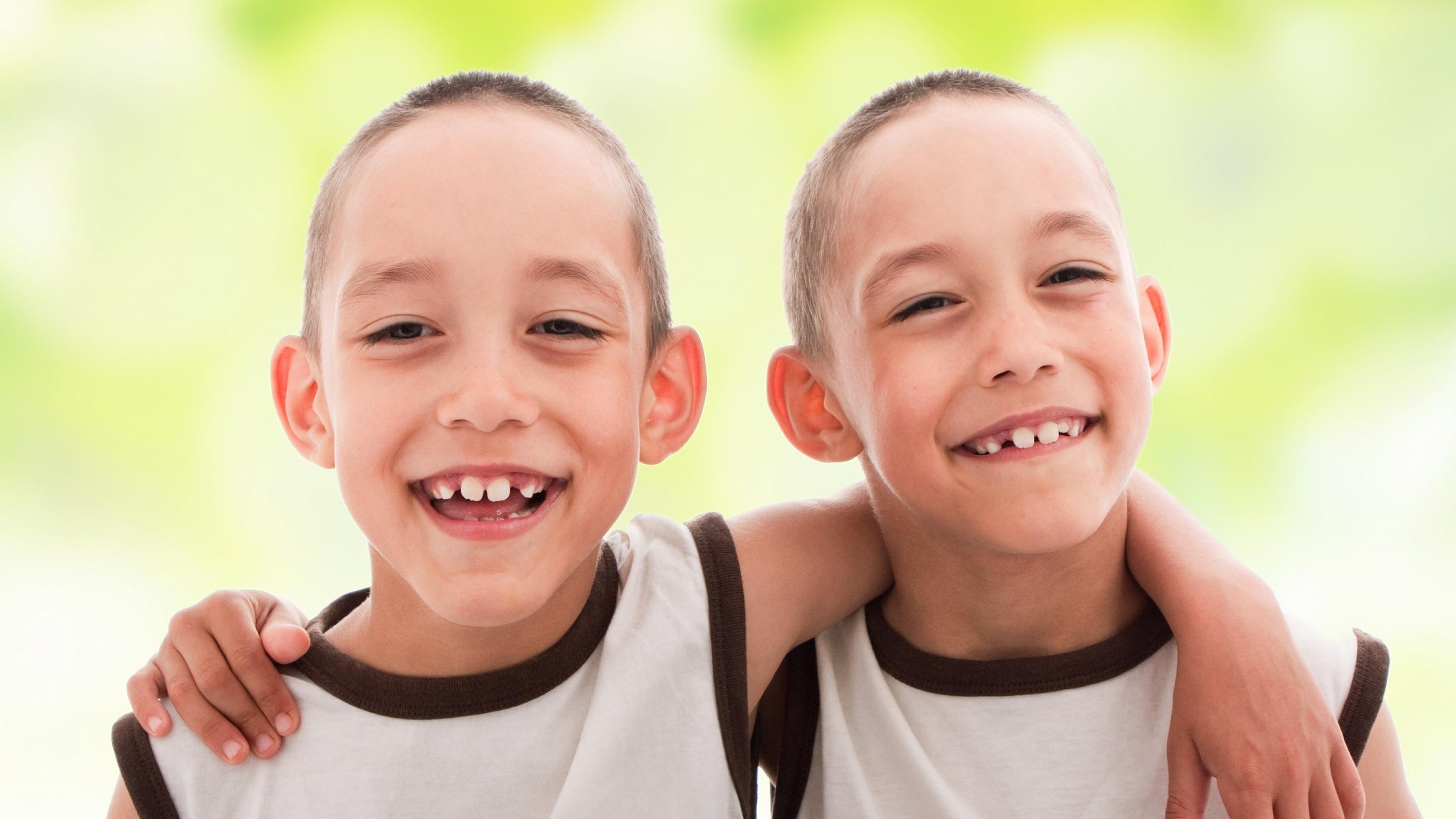 Zwei fröhliche Jungen, die sich so ähnlich sehen, dass es eineiige Zwillinge sein dürften, lächeln in die Kamera.