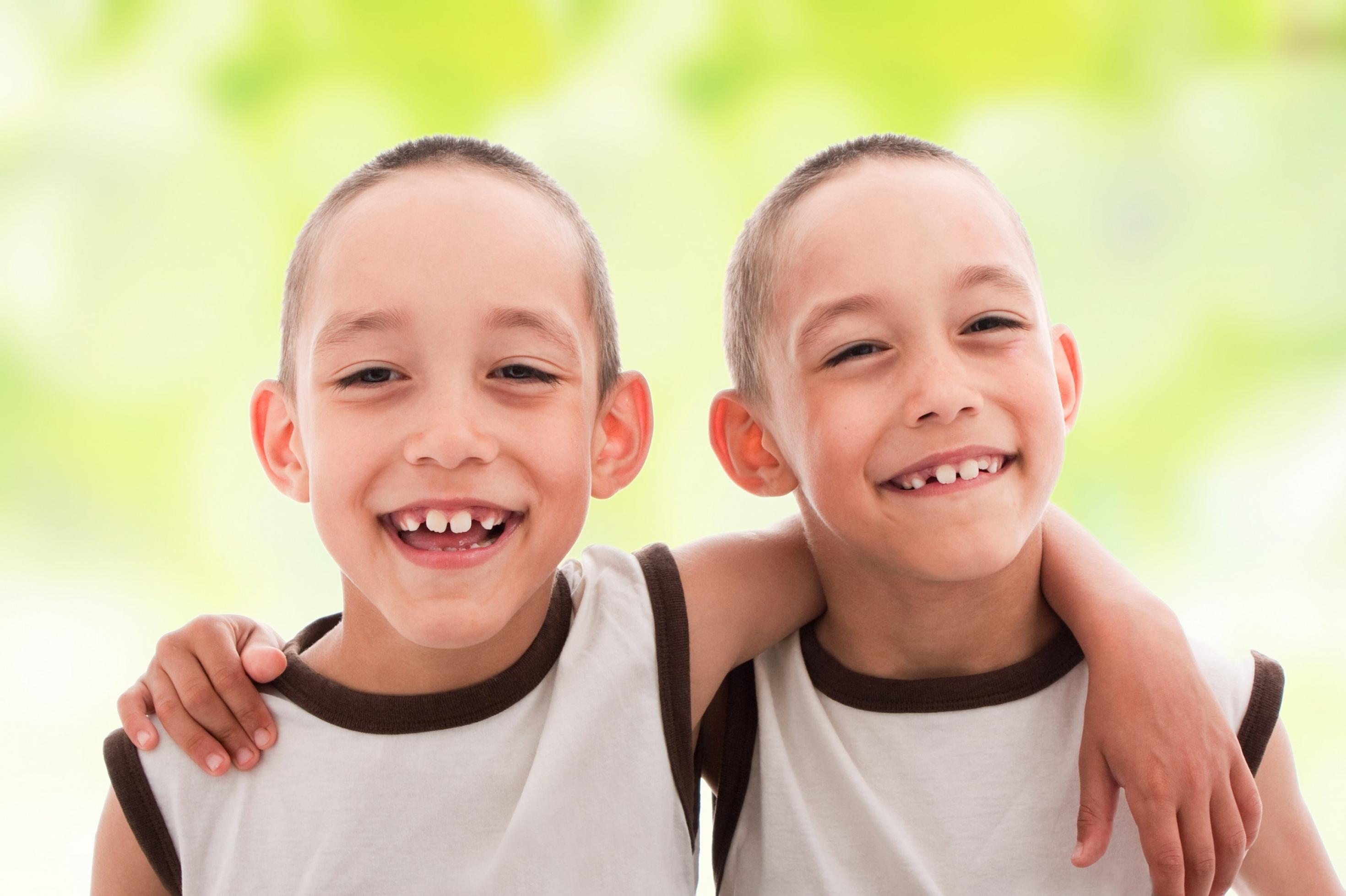 Zwei fröhliche Jungen, die sich so ähnlich sehen, dass es eineiige Zwillinge sein dürften, lächeln in die Kamera.